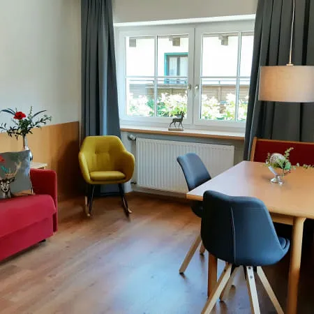 Wohnzimmer mit rotem Sofa, Tisch und Stühlen, Fenster mit Vorhängen