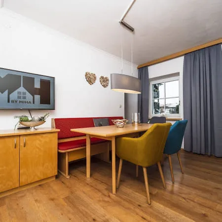 Wohnzimmer mit Holzfußboden, TV, Tisch und bunten Stühlen