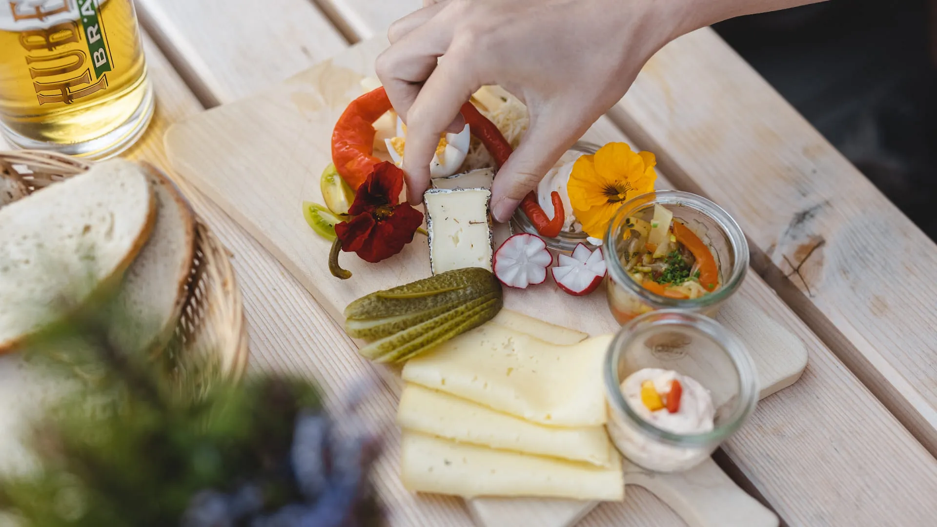 Brett mit Käse, Gemüse und Blumen auf Holztisch