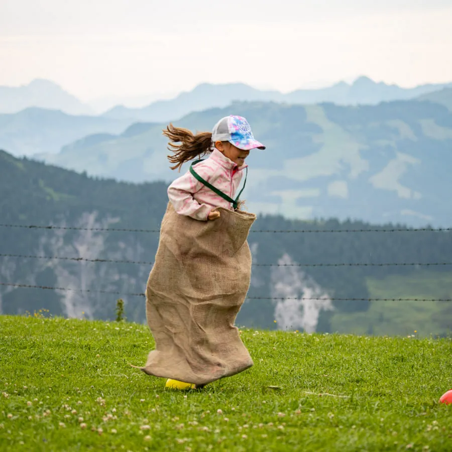 Ein Kind springt in einem Sack auf einer Wiese.